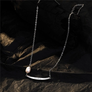 Minimalist silver pearl necklace with Freedom engraved curved pendant on black background