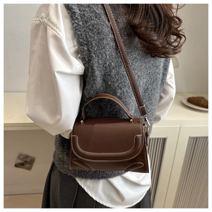 Detail shot of a dark brown crossbody bag on a model wearing a classic style outfit