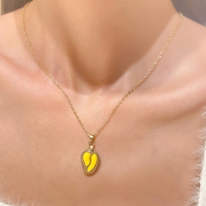 Macro detail of gold-plated necklace with a vibrant yellow mango-shaped pendant charm