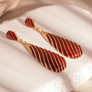 Detail of vintage gold-plated teardrop earrings with deep red enamel and slanted zebra patterns