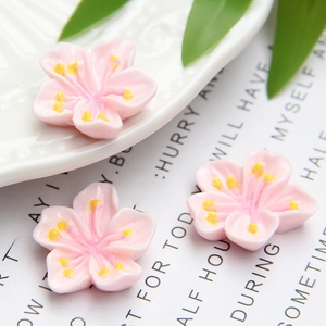 Macro detail of three pink resin cherry blossom DIY charms with yellow centers