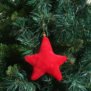 Red plush star Christmas tree ornament with golden hanging string on green pine branches