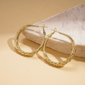 Close-up of gold metal hoop earrings with twisted texture on white marble surface