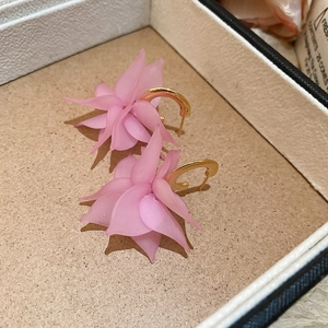 Detail shot of acrylic pink petal C-shaped earrings with gold metal hooks in a jewelry box