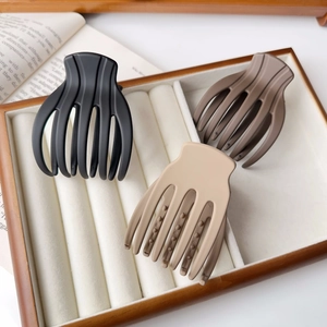 Three large matte hair claw clips in black, dark brown, and beige colors on a wooden tray