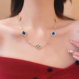 Close-up of a gold-plated necklace with five blue and gold clover motifs on a model