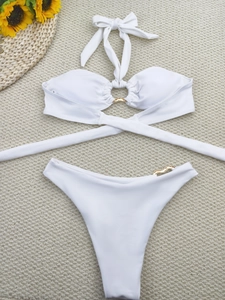 Flat lay of white bikini set with gold metal accents and wraparound ties on a beach mat