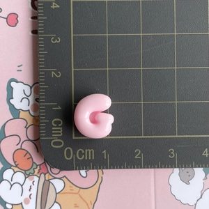 Macro shot of a pink resin G letter hair clip accessory showing 1.5cm size on a ruler