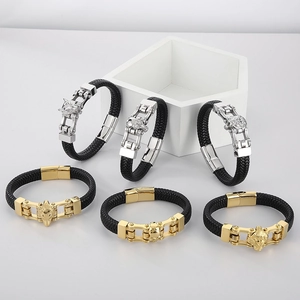 Detail of woven leather bracelets with silver and gold wolf head charms on white surface