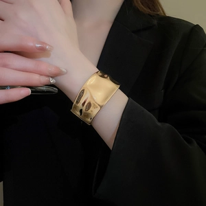 Detail of wide irregular wave-patterned gold metal cuff bracelet on black suit sleeve