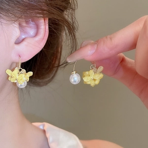 Détail de boucles d'oreilles fleurs jaunes avec une perle blanche et un clou doré