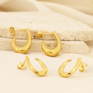 Détail de boucles d'oreilles géométriques dorées en C sur pierre et tissu blanc