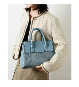 Blue tote bag with crocodile texture detail carried by a model in a beige coat