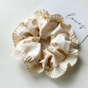 Detailed macro view of champagne satin scrunchie with pleated edges and premium texture