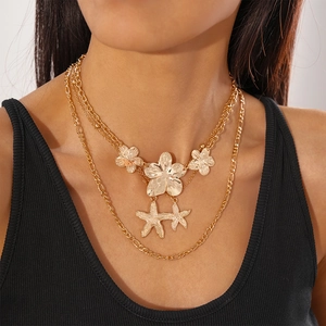Detail of layered gold-tone necklace featuring metallic flowers and starfish pendants