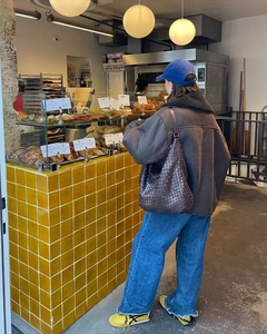 Détail d'une veste en peau lainée foncée et d'un sac en cuir tressé dans une boulangerie