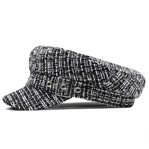 Detail of black and white tweed baker boy hat with square metal buckle and eyelets