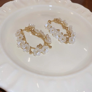 Gros plan de boucles d'oreilles fleurs en acrylique blanc avec perles dorées sur un plateau