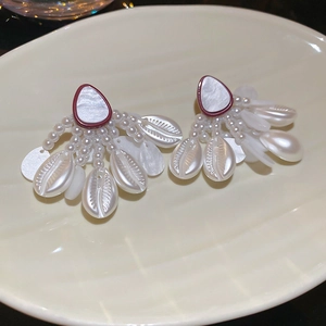 Detail view of shell and pearl tassel earrings with burgundy drops on a textured tray