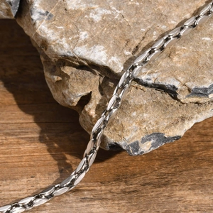 Polished silver stainless steel bracelet with flat almond links on a stone and wood base