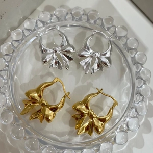 Detail view of gold and silver bow-shaped brass earrings on a clear glass plate