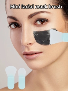 Mini silicone facial mask brush applying clay mask on a model face with tool detail