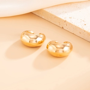 Macro shot of minimalist gold drop earrings on a stone with smooth metal texture