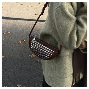 Close-up of brown leather crescent bag with silver rivets and woven strap in autumn setting