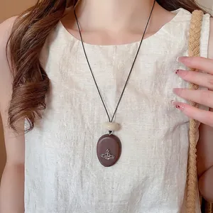 Vintage acrylic and wood Saturn pendant necklace with black cord on beige linen top