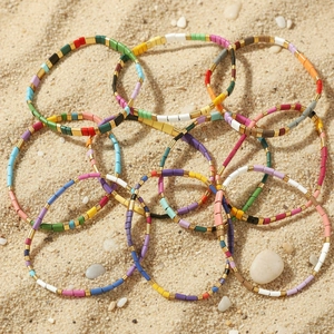 Stack of colorful Tila bead bracelets with gold accents on a beach sand background