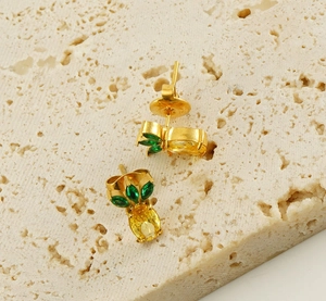Close-up of gold pineapple stud earrings with yellow rhinestones and green marquise gems