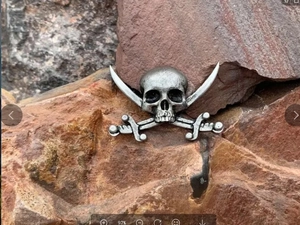 Retro pirate style skull and crossbones metal brooch pinned on a rustic rock surface