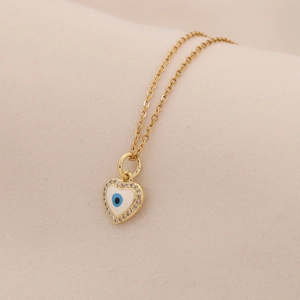 Dettaglio del ciondolo a cuore dorato con occhio blu e cristalli scintillanti