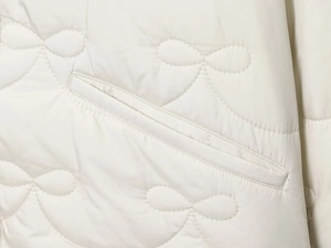 Detail of cream quilted jacket featuring cherry embroidery patterns and side pocket