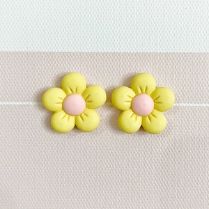 Close-up of yellow frosted resin flower earrings with pink centers on textured background