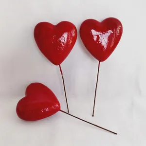 Three bright red heart-shaped cake toppers with long wire stems on white fabric
