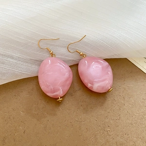 Close-up of pink marble resin oval earrings with gold metal hooks on white soft fabric