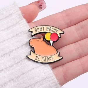 Cute capybara enamel pin with balloons and Don't Worry Be Cappy text on a palm