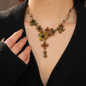 Gros plan d'un collier fleur vintage avec strass orange et verts porté par un mannequin