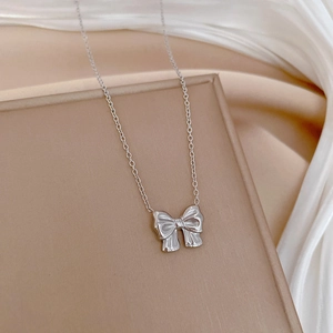 Macro shot of a silver bow pendant necklace resting on elegant white silk fabric