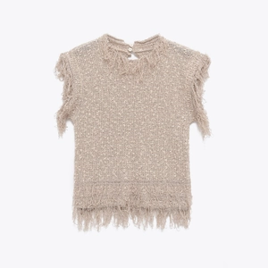 Detail of knitted sleeveless top featuring fringe trim on armholes and hem with button closure