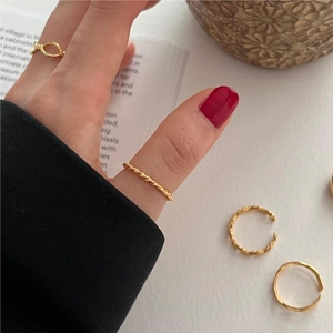 Macro detail of minimalist gold twisted stacking rings worn by a model on a warm background