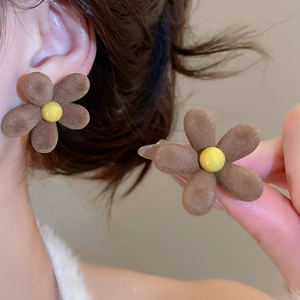 Close-up of brown flocked flower earrings with yellow centers on a model for winter style