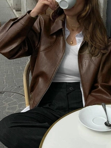 Brown faux leather jacket with lapel and zipper worn by a model in a cozy cafe setting
