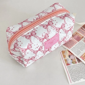 Close-up of quilted cosmetic bag in white with pink bow patterns and a pink zipper