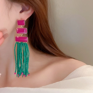 Detail of bohemian tassel earrings with magenta enamel and green seed beads on model