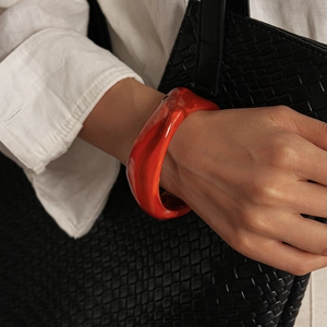 Détail d'un bracelet manchette en résine orange avec texture sable et tenue élégante