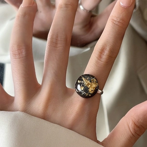 Detail of a silver ring with a black round resin face and embedded gold foil flakes