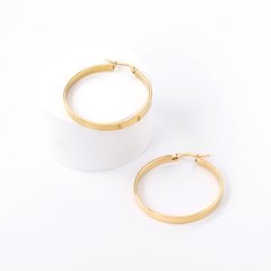 Detail view of large gold stainless steel hoop earrings on a minimalist white prop