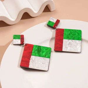 Close-up of geometric acrylic earrings in red green and marble white on a ceramic plate